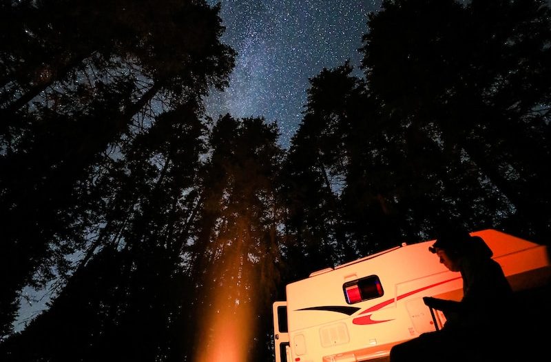 a camper parked in the woods at night with the stars in the sky