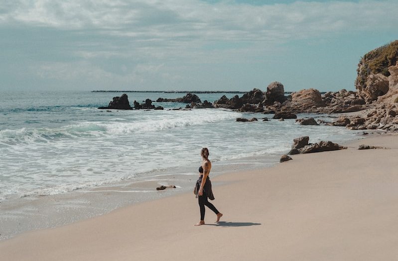 a woman walking along a beach next to the ocean