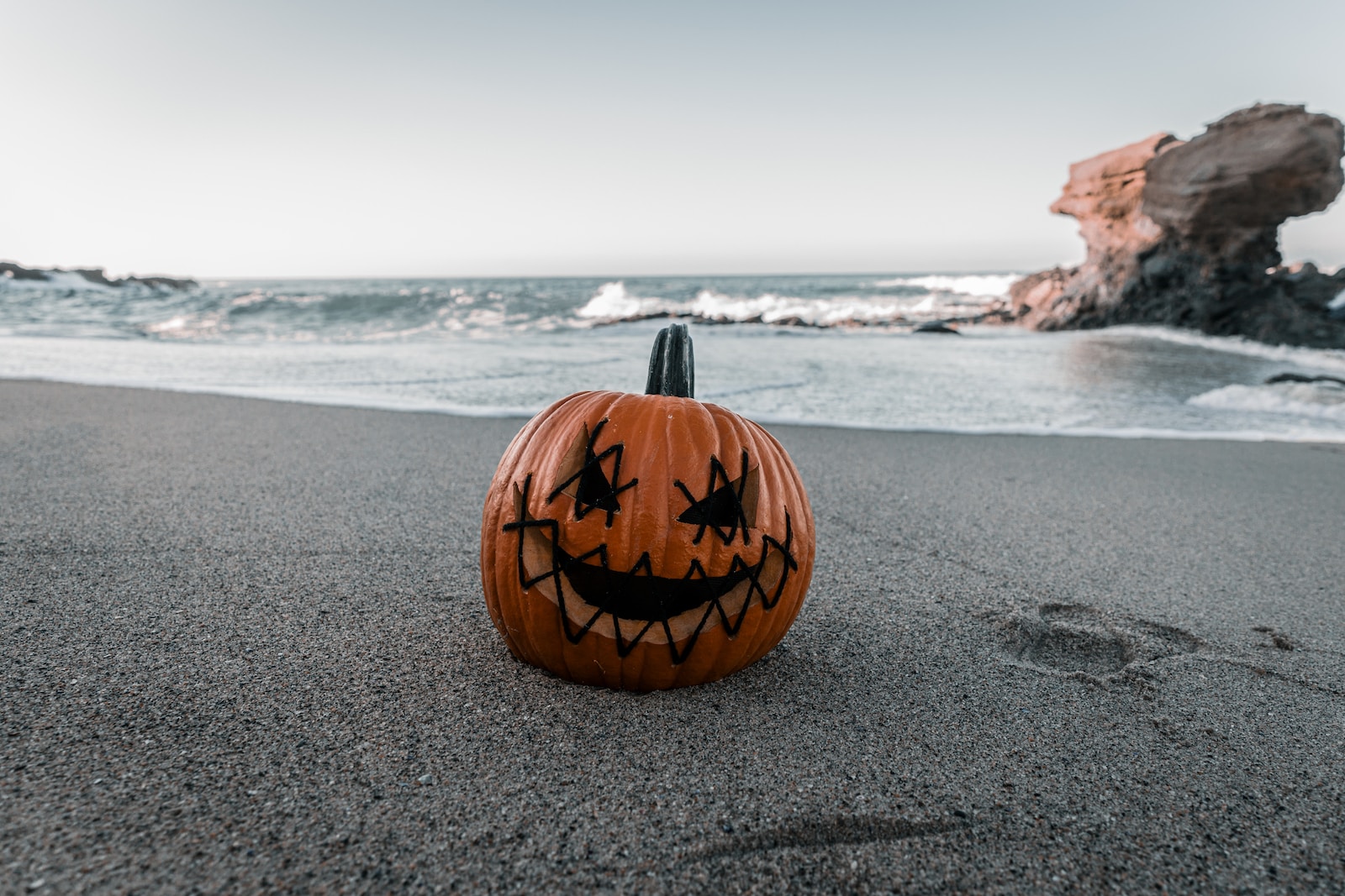 a carved pumpkin sitting on top of a sandy beach